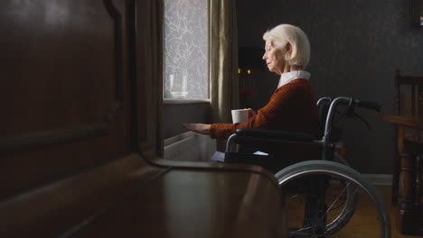 Senior-Woman-In-Wheelchair-Trying-To-Keep-Warm-By-Radiator-During-Cost-Of-Living-Energy-Crisis