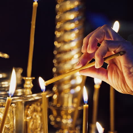 woman's hand lighting a candle and putting it among other candles in a church. candles are lit for prayer intentions.