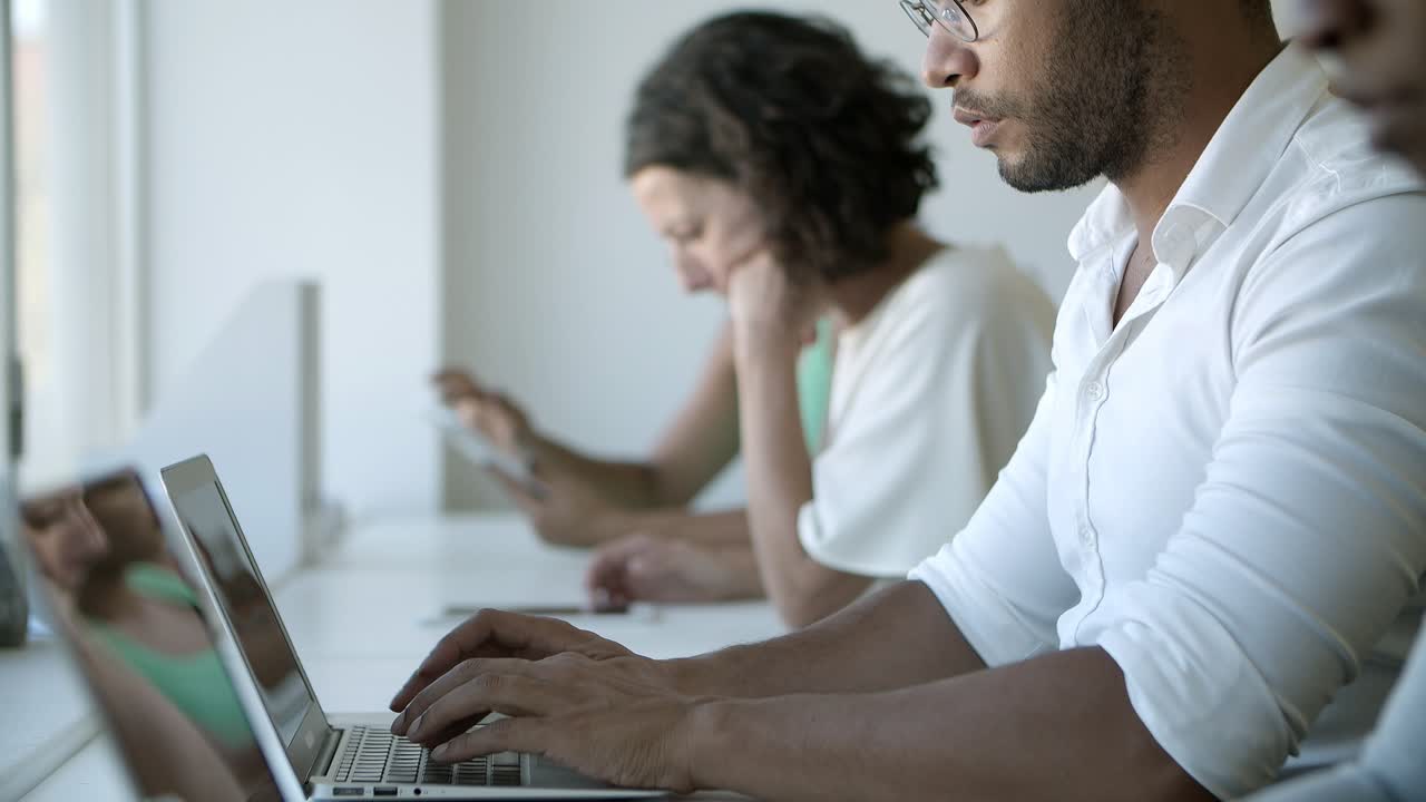 vista lateral de un hombre afroamericano con gafas escribiendo en una computadora portátil
