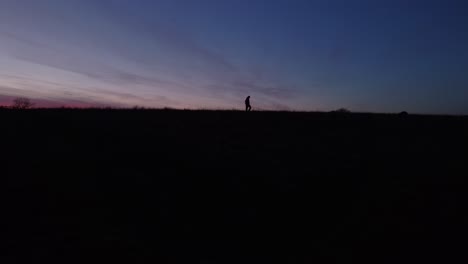 man walks along hill after dusk, silhouetted