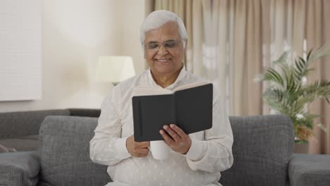 happy indian old man reading book and drinking tea