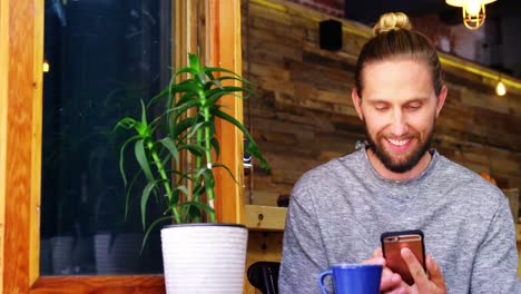 Un-Hombre-Guapo-Usando-Un-Teléfono-Móvil-Mientras-Toma-Un-Café