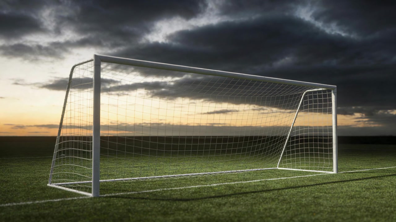 Kaydırılan kamera, alacakaranlıkta sahayı dolduran beyaz futbol kalesini ve ağını gün batımı ışığına karşı gösteriyor.