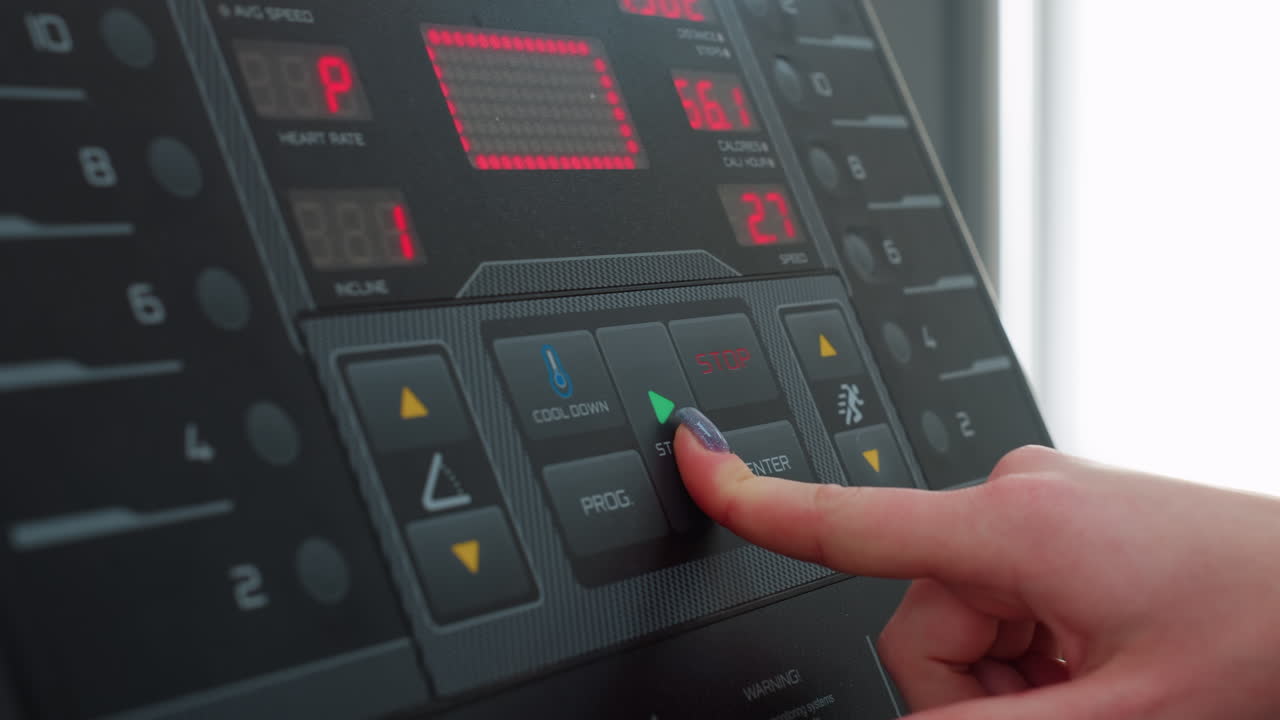 close up fair skinned hand with polished nail pressing start button on treadmill console displaying workout metrics like speed and calories under bright natural gym light