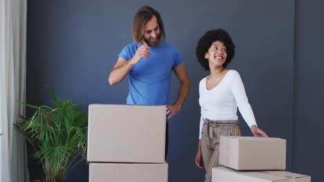 Mixed-race-couple-standing-in-between-cardboard-boxes-at-new-apartment-house