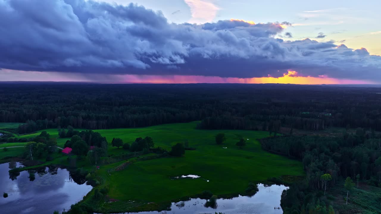 Dramatic storm clouds roll in over green fields and forests as the sun sets in the European countryside