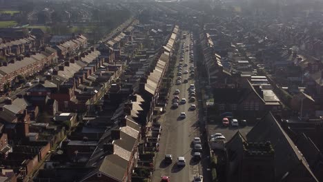 La-Vista-Aérea-Descendente-Revela-Hileras-De-Históricas-Casas-Adosadas-En-Dentons-Green,-St-Helens,-Con-Un-Largo-Camino-Que-Conduce-Hacia-La-Bulliciosa-Ciudad-Al-Amanecer