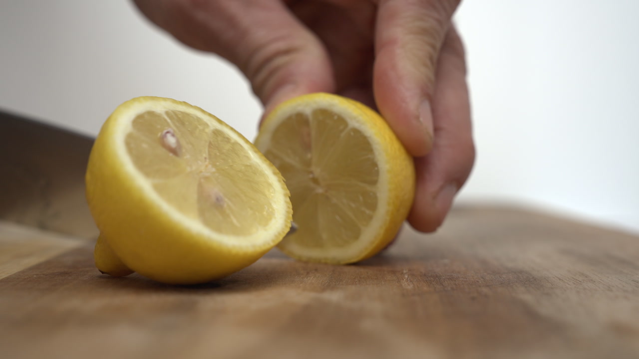 Slow motion video of a knife slicing a fresh yellow lemon in half on a wooden cutting board against a clean white background