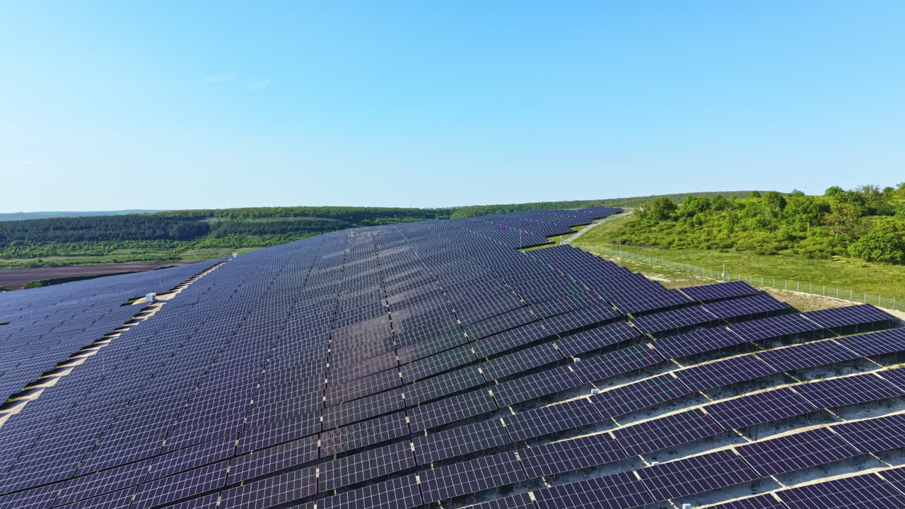 Stor solcellepark i et landområde med solceller opstillet i rækker under en klar blå himmel om dagen.