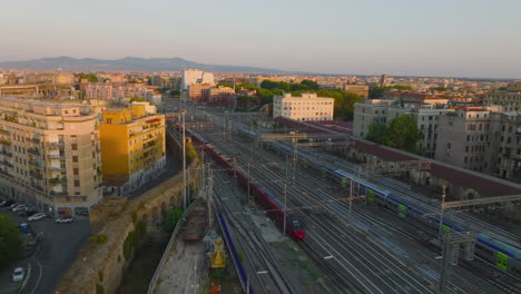 Passenger-trains-driving-on-multitrack-railway-lines-in-city.-Multistorey-residential-buildings-lit-by-evening-sun.-Rome,-Italy