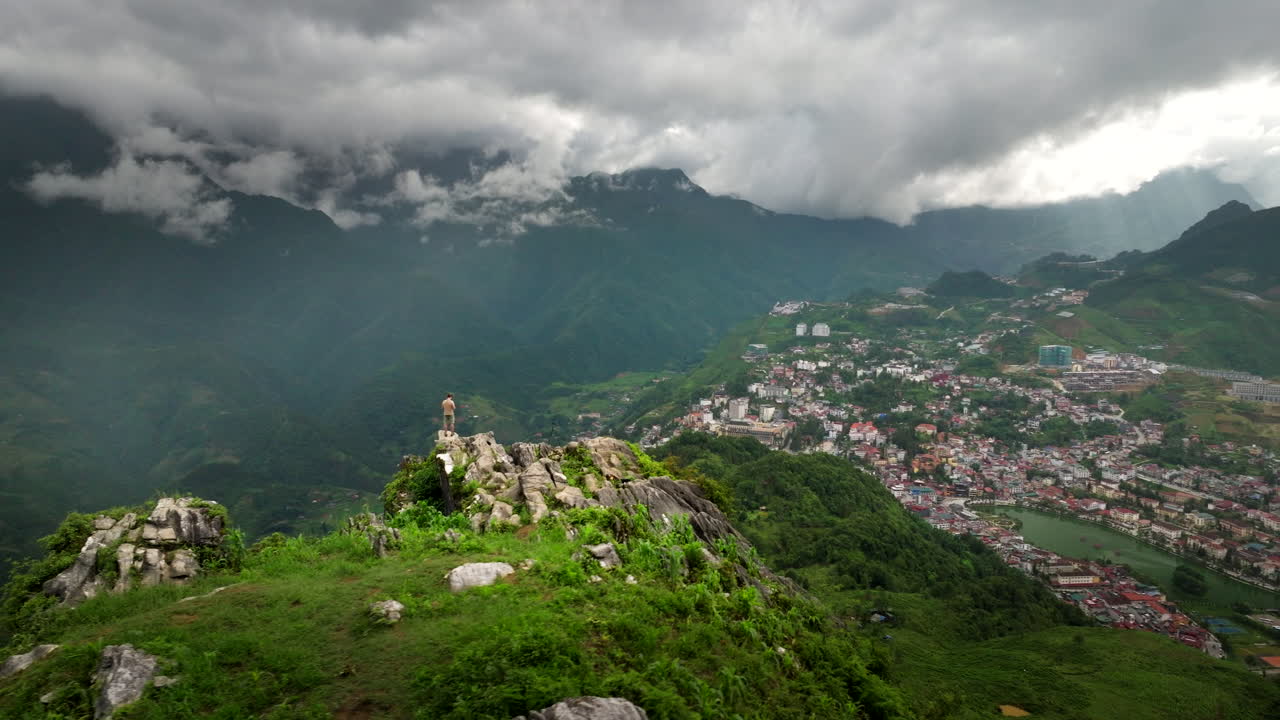Man stand atop Ha Rong mountain overlooking Sapa town scenic mountainous terrain
