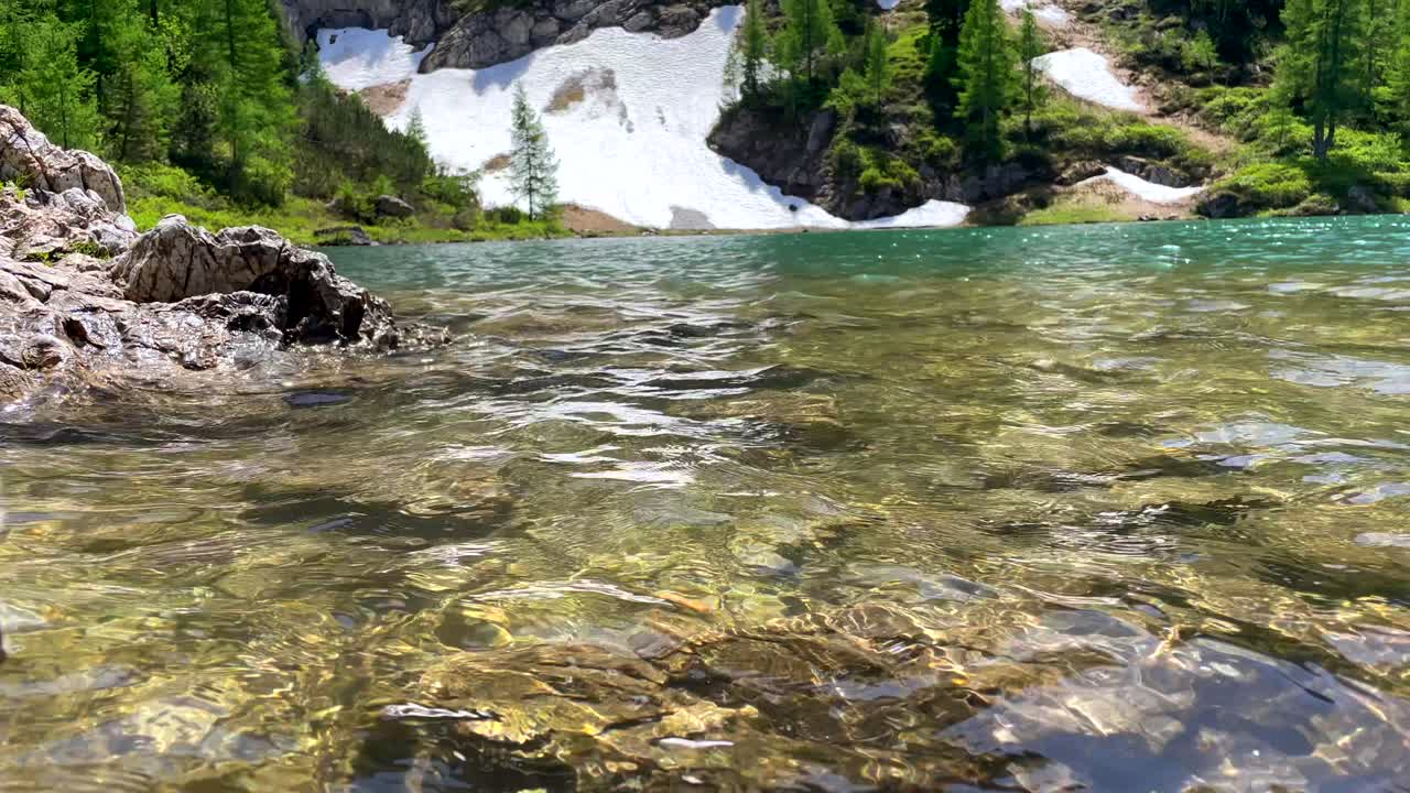 Low angle shot of clear fresh mountain lake in sunlight and snowy shore in background