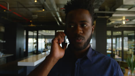 Front-view-of-young-black-businessman-talking-on-mobile-phone-while-walking-in-a-modern-office-4k