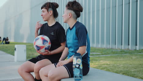 two female soccer athletes sitting on street bench and chatting