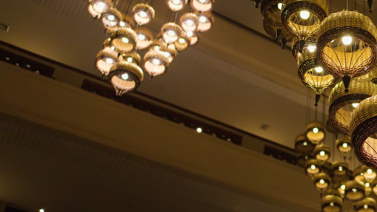 Warm wicker chandeliers glow overhead in a traditional Thai luxury hotel, camera pans upward smoothly