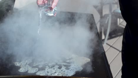 pouring water on the flat top griddle to clean and steam off the cooking surface in slow motion