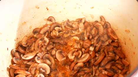 sautéing mushrooms in an enamel dutch oven pot - mushrooms frying and bubbling on the stove - close up top down view