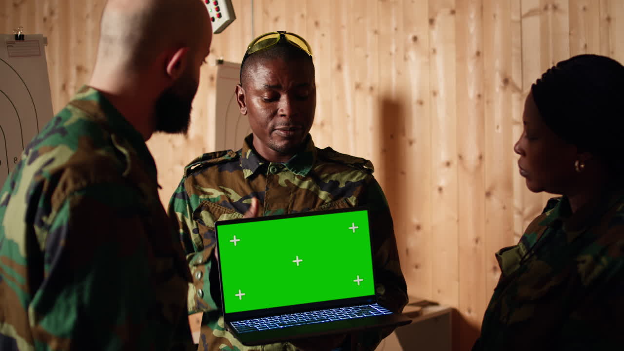 Team of military units at shooting range watching video on green screen tablet