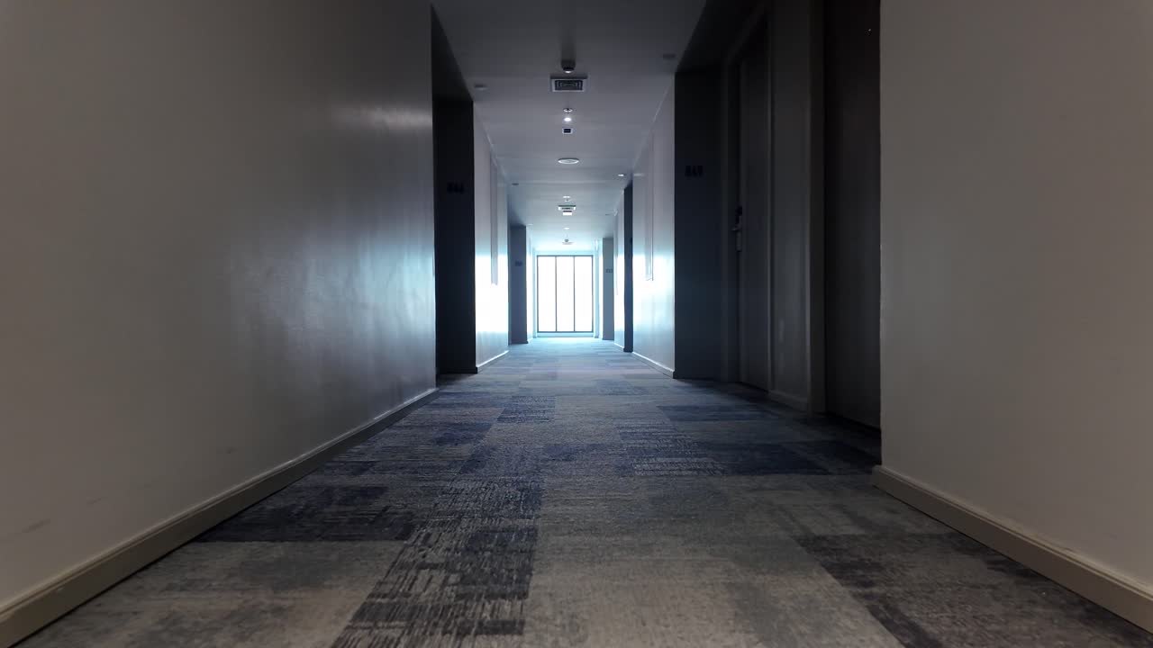 Dim hotel hallway stretching toward a bright exit, creating a calm, empty passageway with perspective