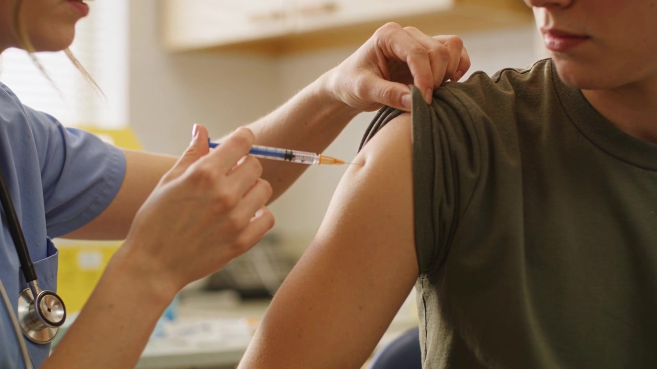 Patient pulling sleeve in clinic while nurse in scrubs inserting syringe for vaccine, stethoscope