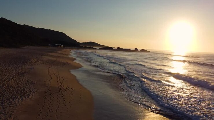 Vista de drone de praia vazia durante o pôr do sol com ondas quebrando na costa