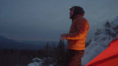 tourist drinking tea by camping tent on mountain top in evening