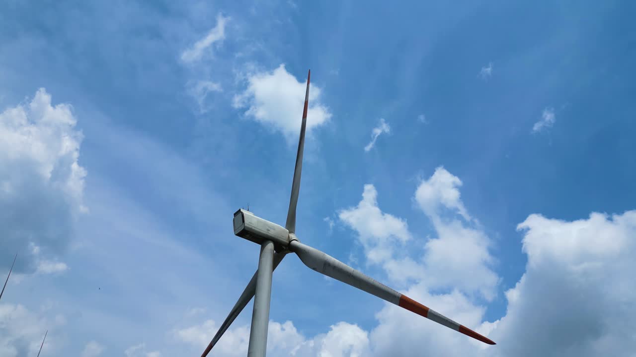 Aerial view of Large wind turbine against blue cloudy sky, global renewable energy