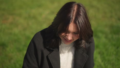 cheerful woman smiling with wind gently fluttering her hair, focusing on something in the background, surrounded by greenery in a peaceful outdoor environment