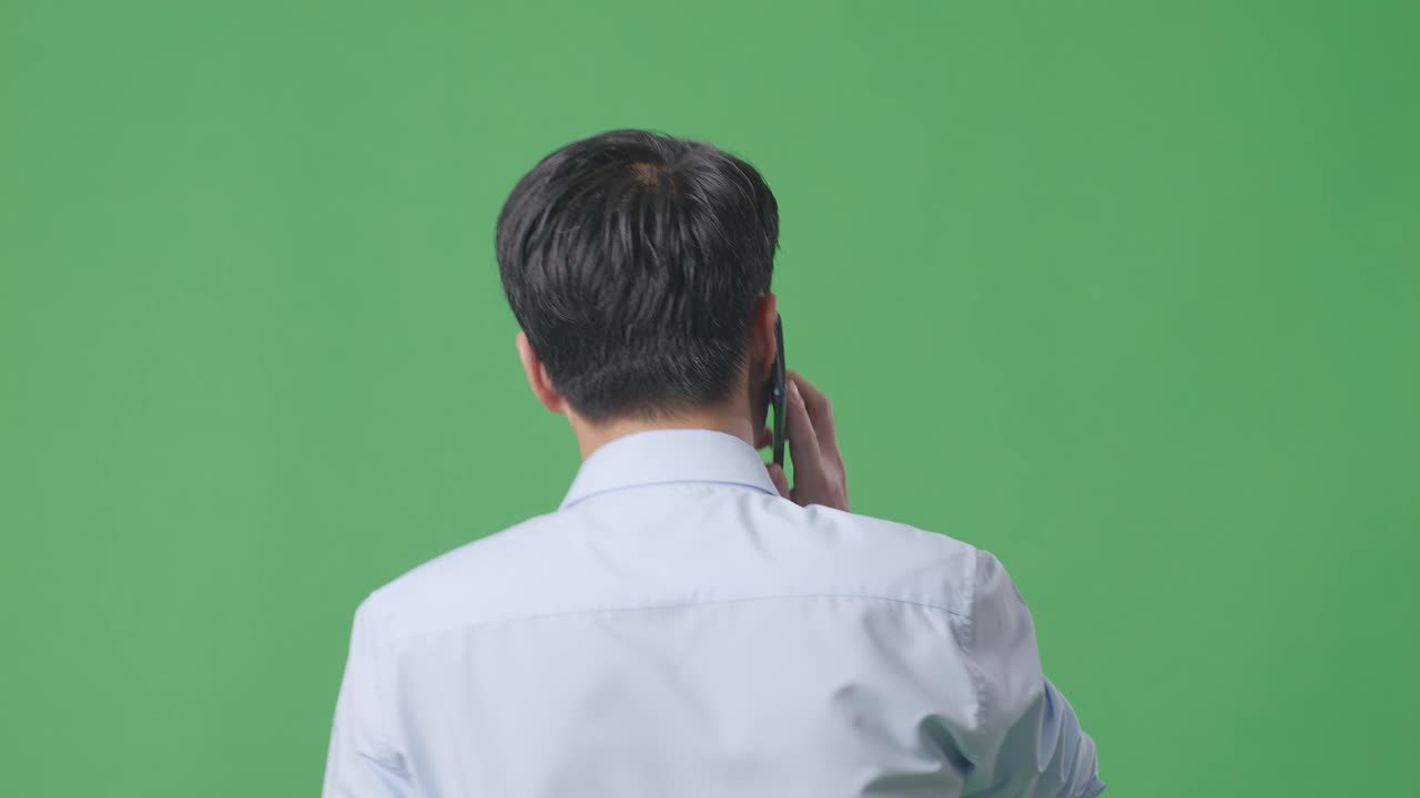 스튜디오의 녹색 화면 배경에서 는 동안 휴대 전화로 이야기하는 아시아 사업가의 뒷면