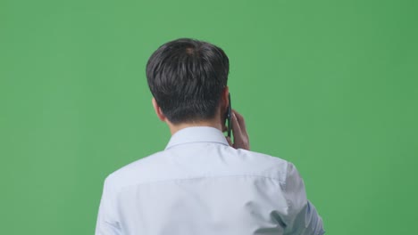 back view close up of asian business man talking on mobile phone while walking on green screen background in the studio