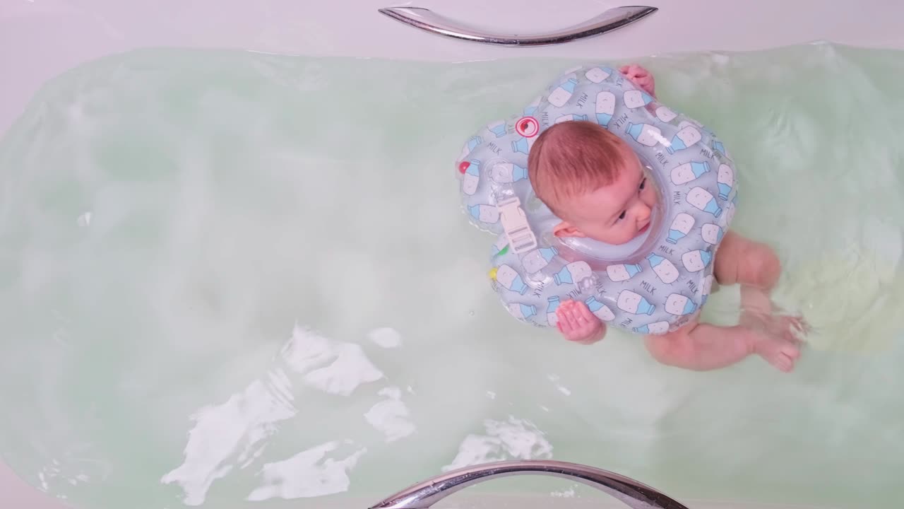 목에 고무 반지를 달고 욕조에서 수영하는 동안 웃는 행복한 아기 아기.