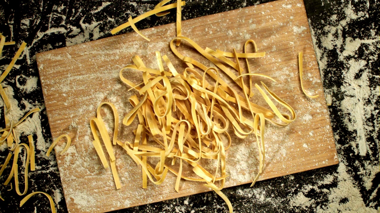 Pasta fresca fatta in casa che cade su un tagliere infarinato