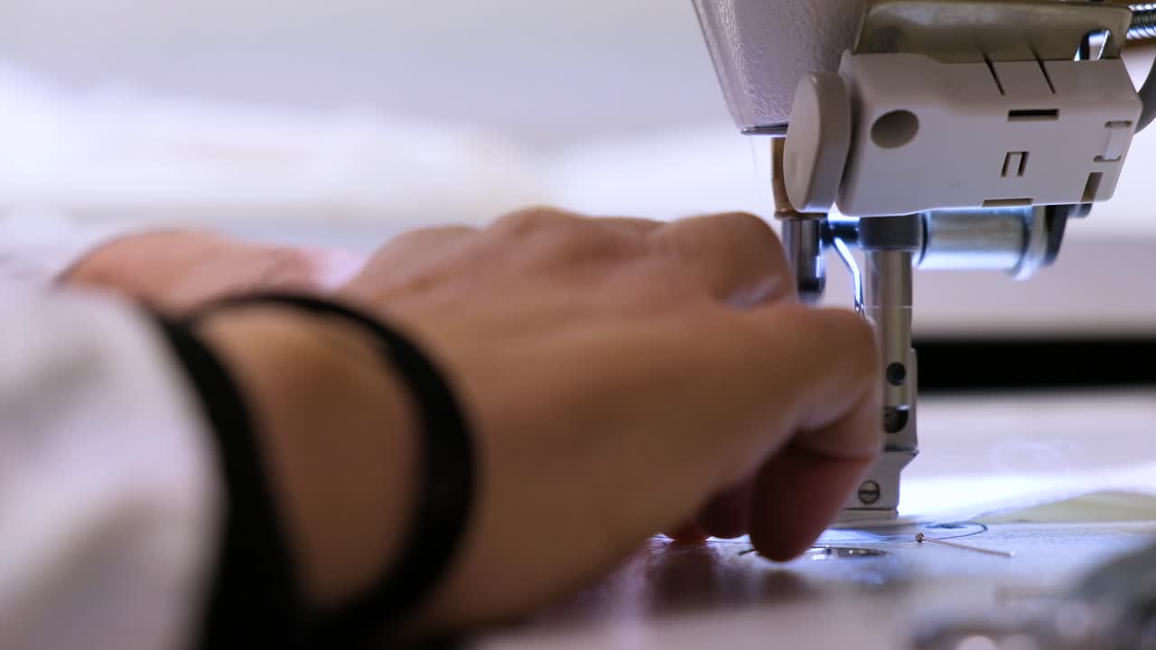 A Close-Up Of Dressmaker's Hands Making Stitching White Cloth On The Sewing