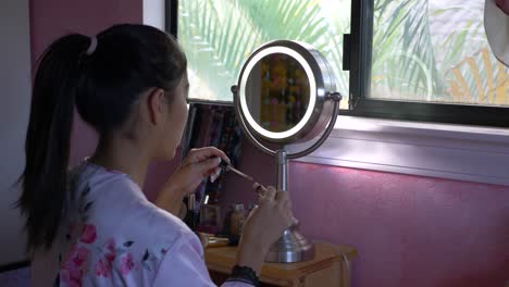 Female-putting-on-makeup-in-front-of-vanity-mirror-with-camera-sliding-left