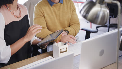 Midsection-of-diverse-male-and-female-colleagues-at-desk-using-tablet-and-laptop,-slow-motion