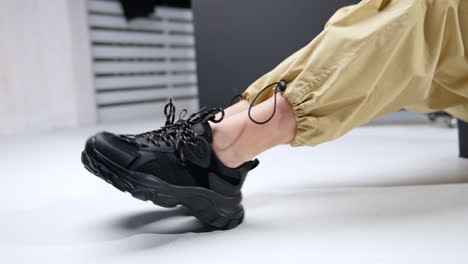 black trendy massive sneakers on female feet. woman wearing beige broad pants sits on the floor demonstrating her sport shoes.