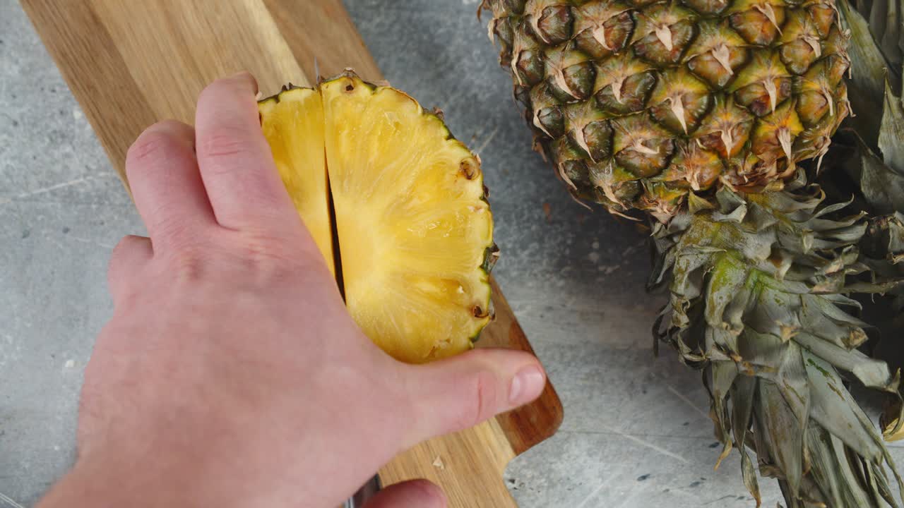 남자의 손은 파인애플 조각을 반으로 잘라습니다.