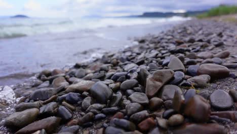 Beautifully-shaped-rocks-laying-on-shore-of-lake-Taupo-in-New-Zealand,-slowmo