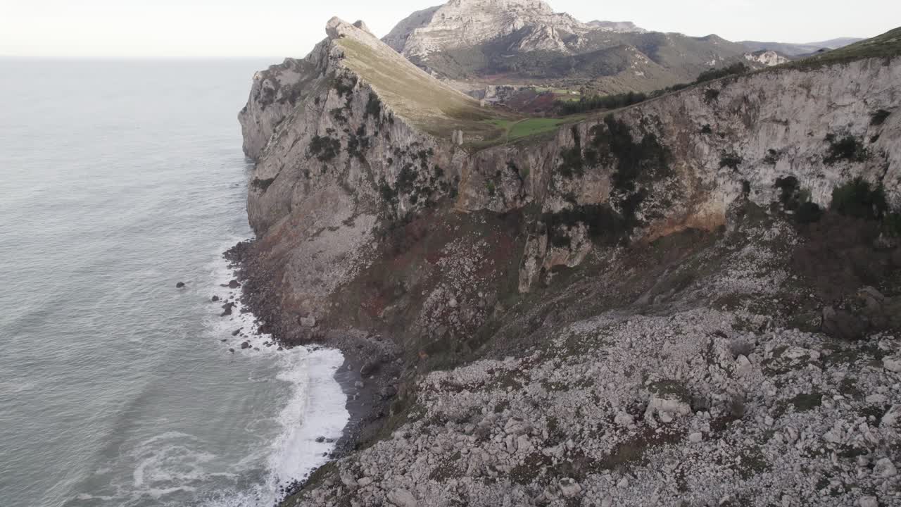 Rocky cliff washed by wavy endless sea on cloudy day. Cantabria, Spain