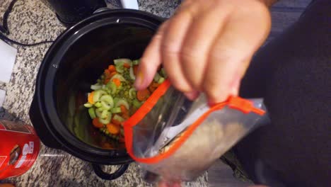 cocinar un guiso en una olla de cocción lenta mirando hacia abajo en la olla y revolviendo los guisantes, zanahorias y otros ingredientes