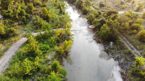 Quickly-flying-up-the-river-at-sunset,-road-on-the-left-parallels-the-river