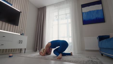 A-sporty-beautiful-woman-performs-a-stand-on-her-head-and-hands-at-home.-On-the-carpet-of-his-own-apartment.-Balance-exercises