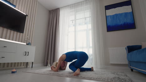 una mujer hermosa deportiva realiza un soporte sobre su cabeza y manos en casa. en la alfombra de su propio apartamento. ejercicios de equilibrio