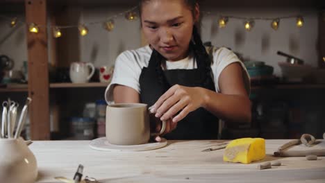 joven alfarera tratando en un mango de arcilla húmeda a una taza