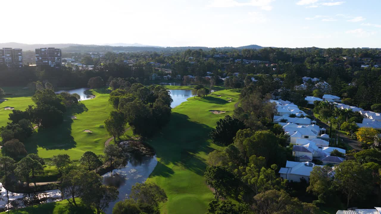 Drone footage captures a serene golf course with lush greenery and adjacent residential area under bright daylight