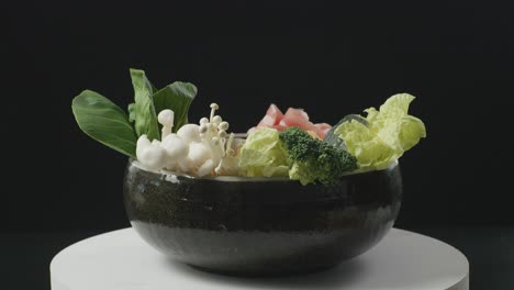 close up of a pot of shabu ingredients spinning around on white table in the black background kitchen