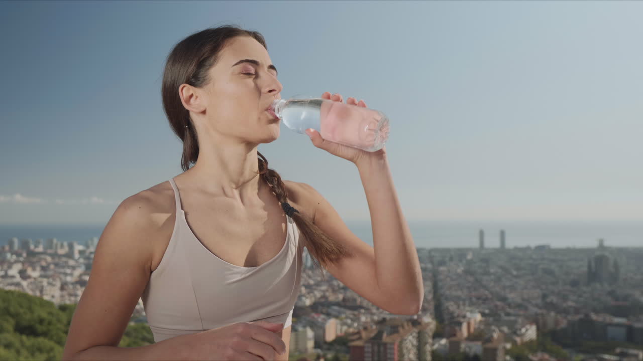 mujer abriendo una botella en el punto de vista de la ciudad. niña bebiendo agua después del entrenamiento