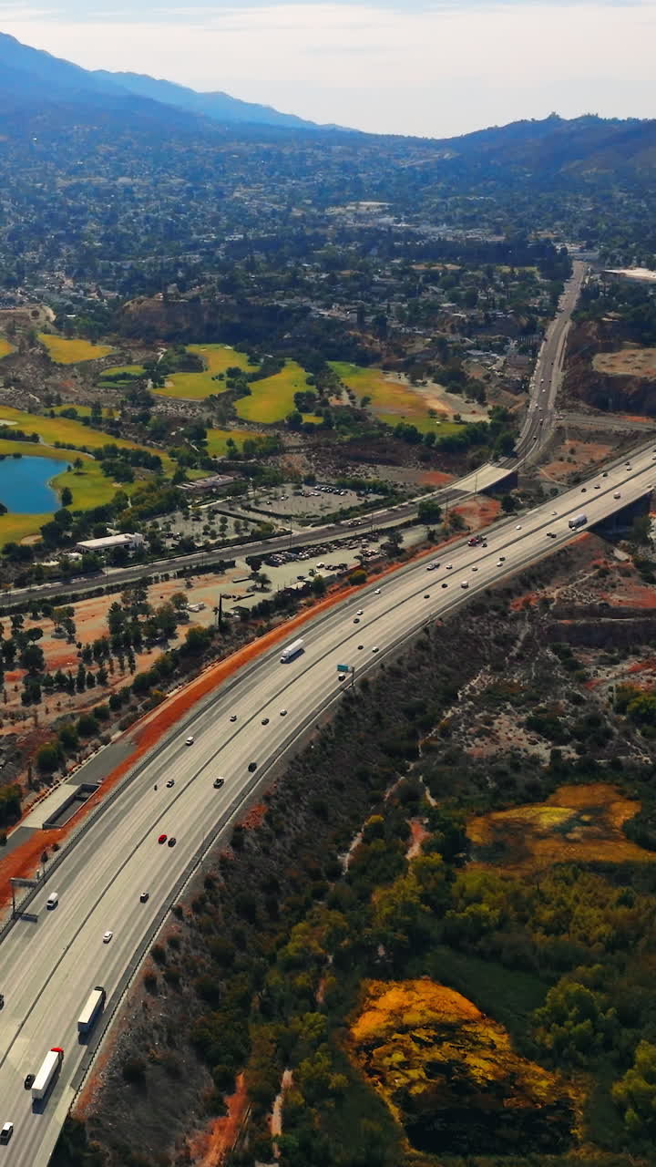 Unusual scenery of Los Angeles outskirts with highway going through. Mountains at backdrop. Aerial perspective. Vertical video