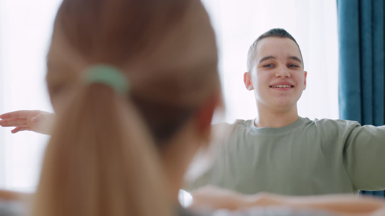 Primer plano de una mujer vista desde atrás que guía a un niño en un estiramiento de brazos durante una sesión de entrenamiento en interiores con una cortina de fondo, mientras el niño levanta los brazos mostrando concentración, disciplina y entrenamiento.