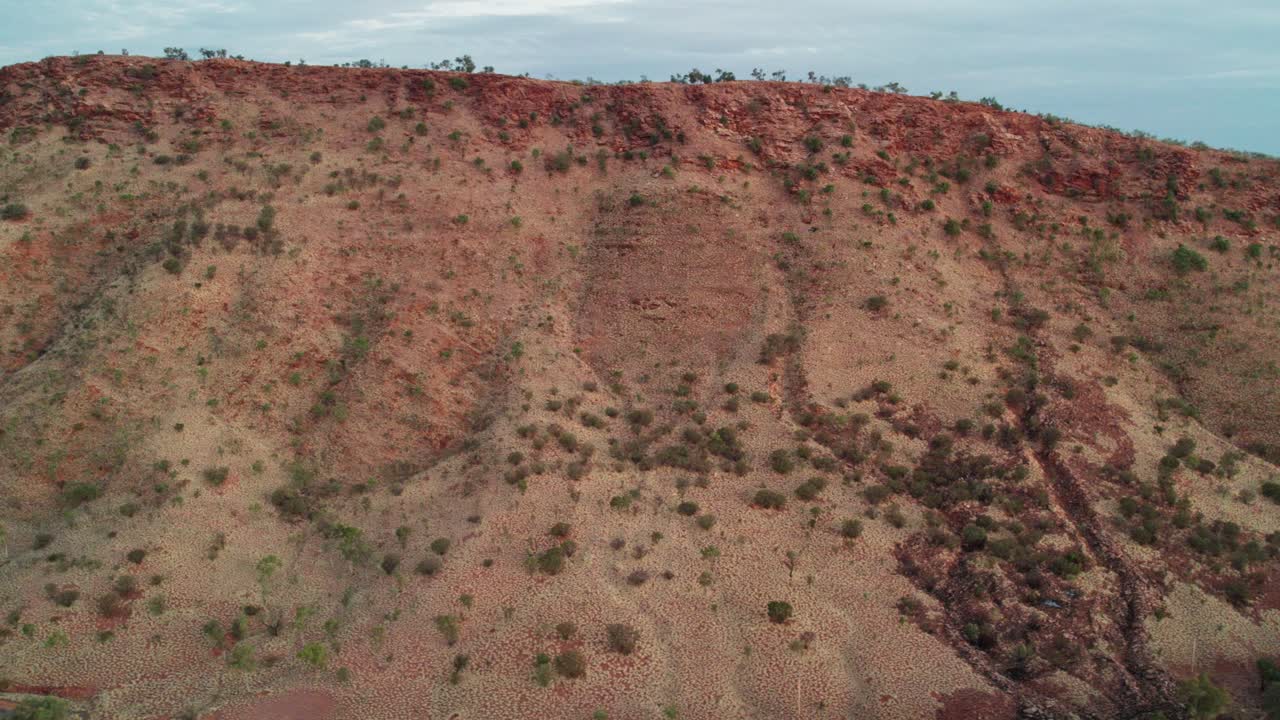 Sideways aerial view of the MacDonnell Ranges near Heavitree Gap, Alice Springs, Mparntwe, with late afternoon sun shining on them. Northern Territory, Australia. August 2022.
